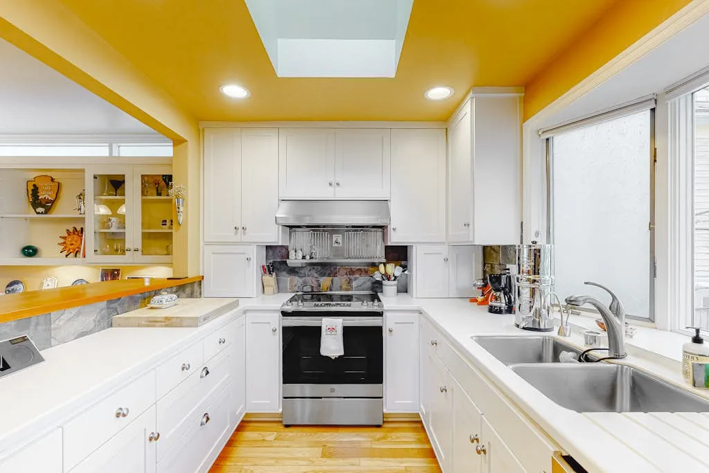 A bright kitchen with white cabinets, a central oven, and a sink beneath the window.
