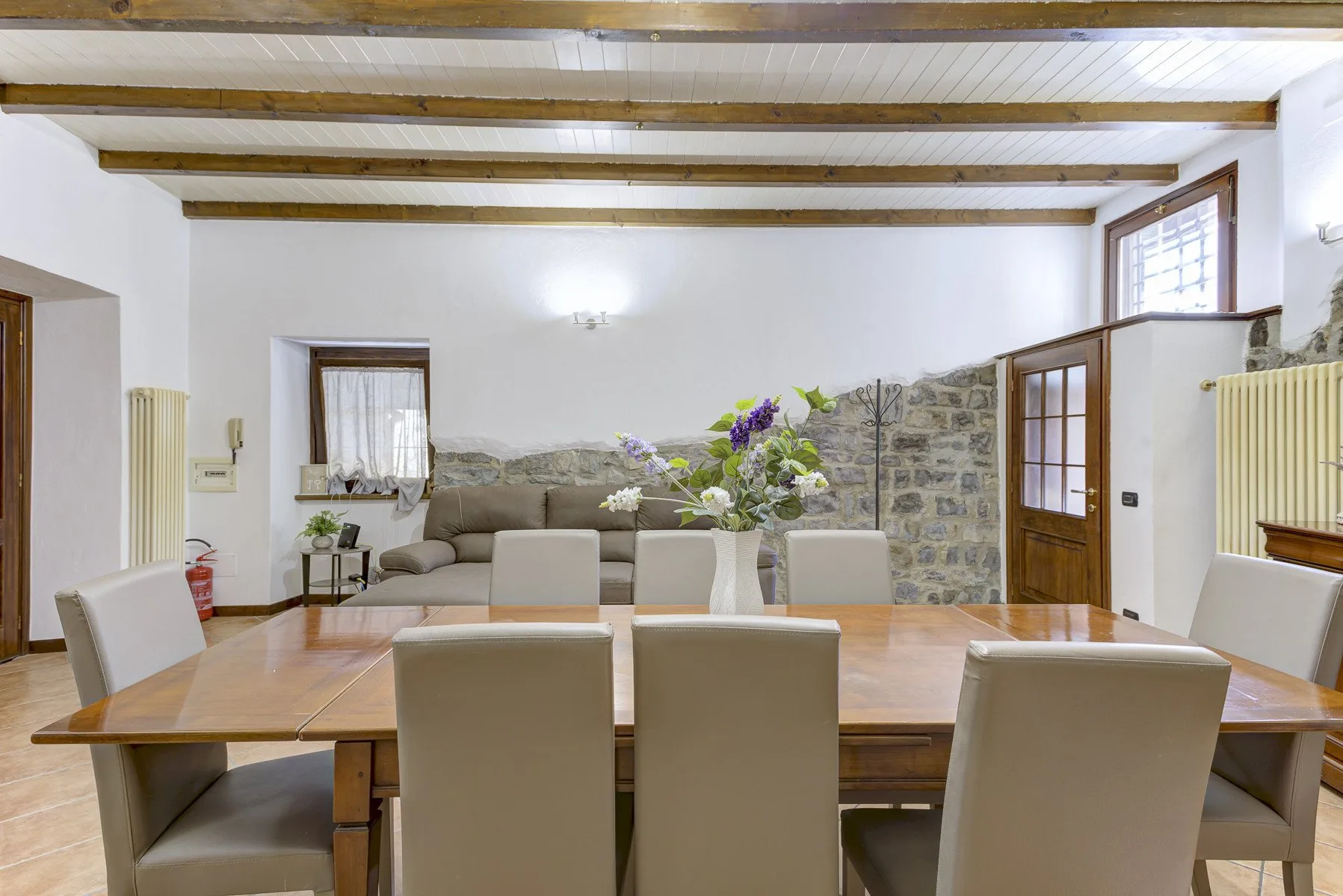 Comedor con una mesa larga de madera, asientos tapizados y vigas expuestas en el techo.