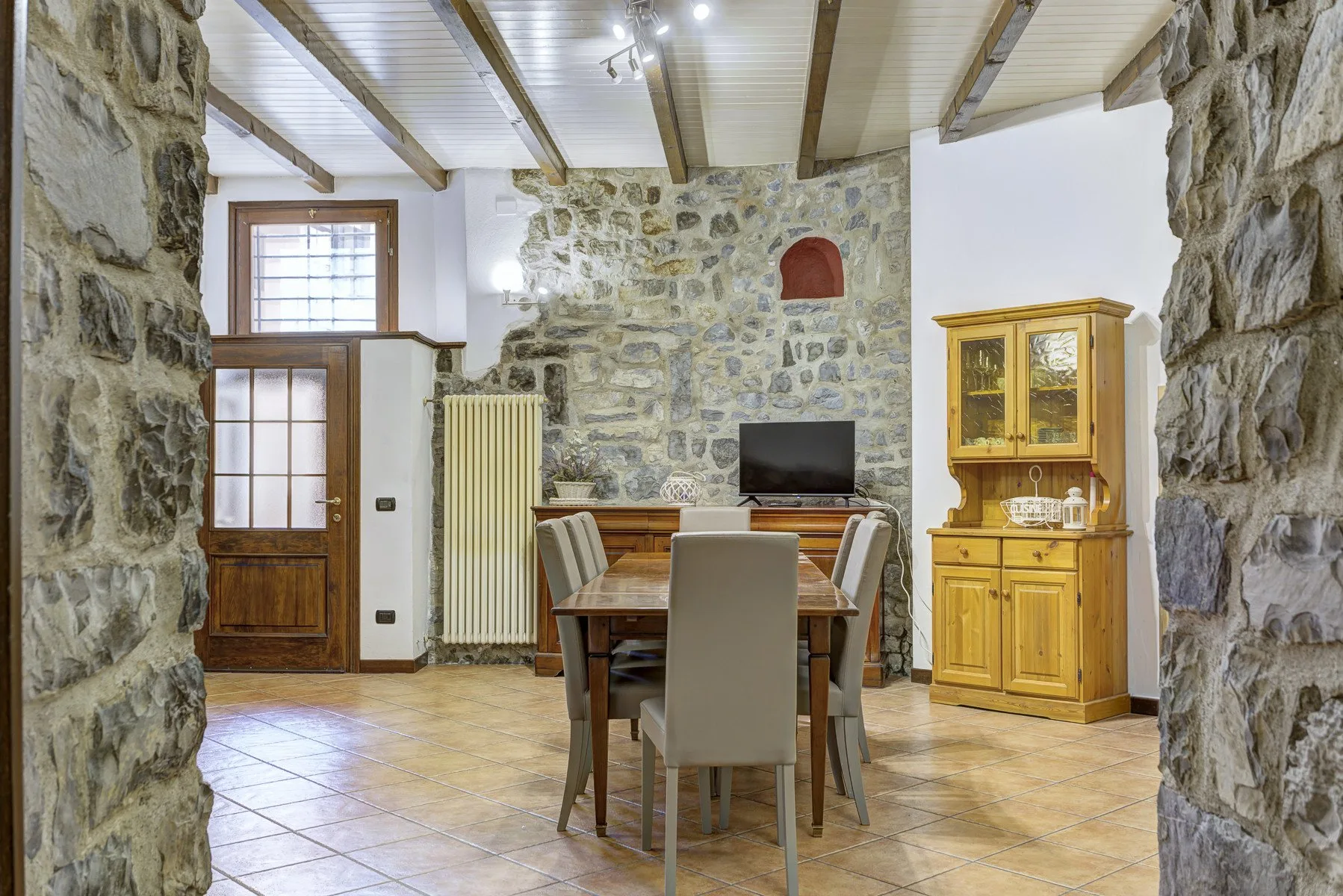 Un comedor rústico con una mesa de madera, sillas y una pared de piedra.