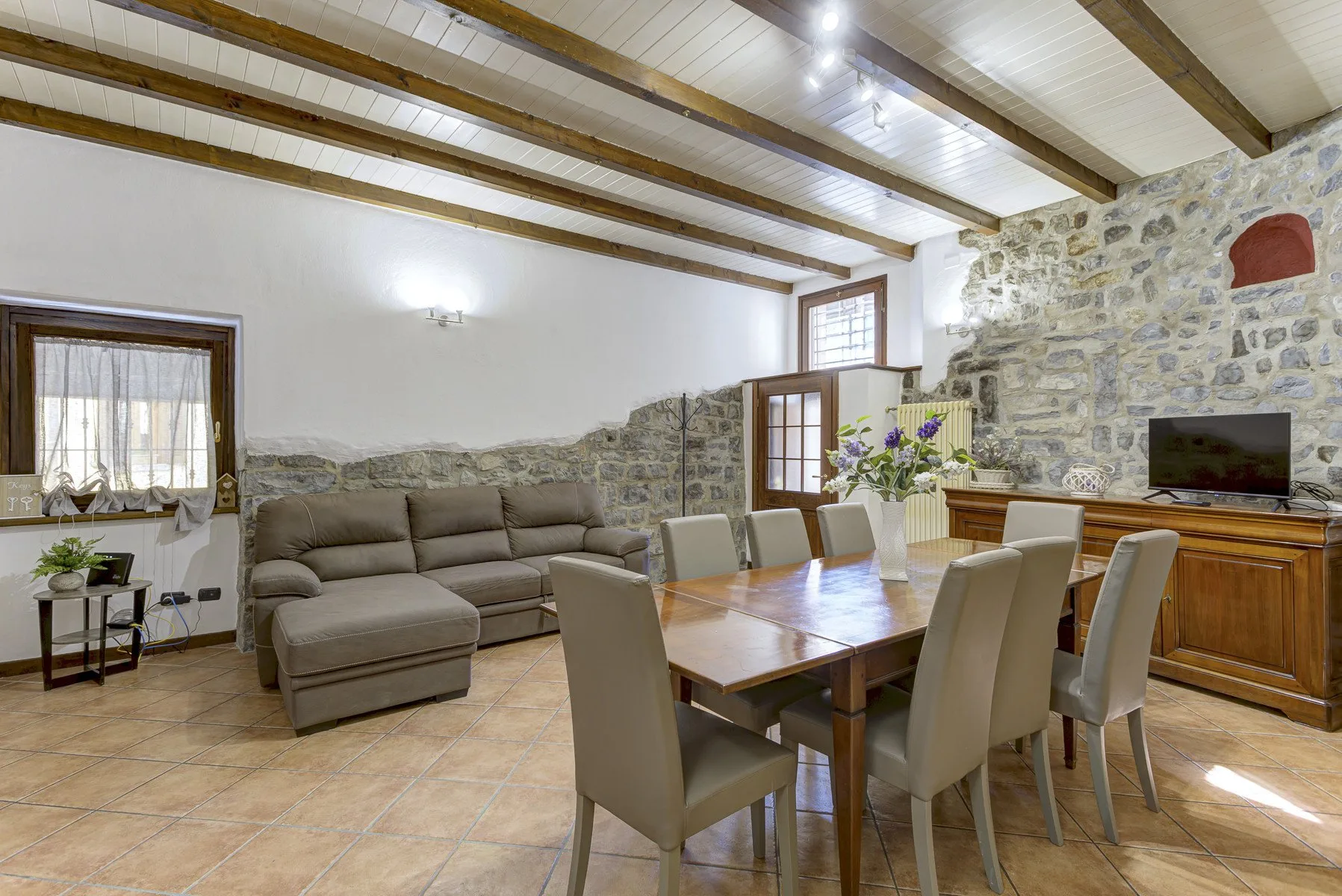 Zona de comedor y estar con una mesa de madera, asientos y una pared de piedra.