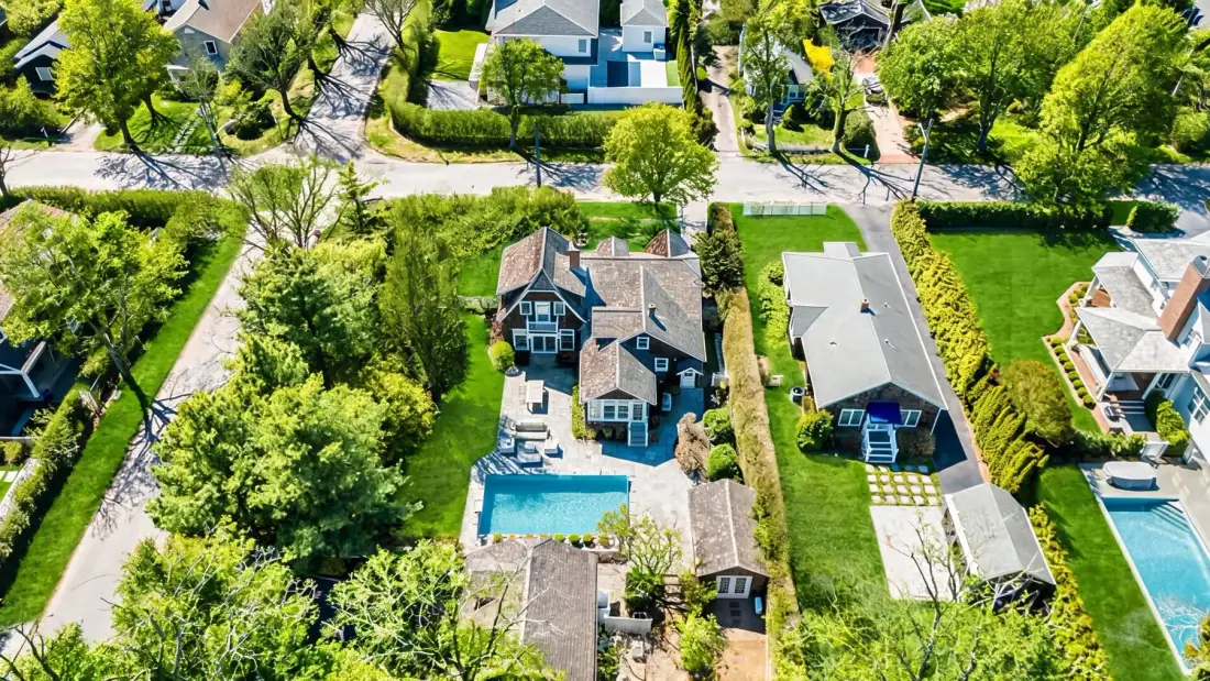Aerial view of houses and green yards, with a swimming pool beside one home.
