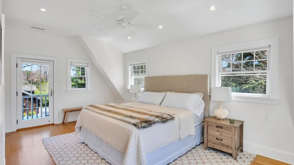 A bright bedroom with a bed, bedside tables, and windows.