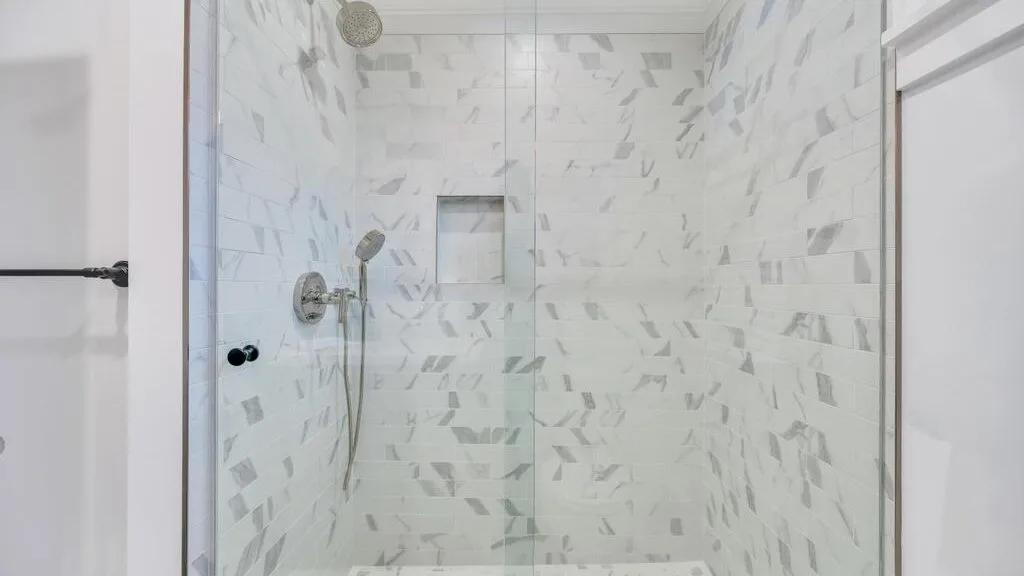 A tiled shower with a handheld showerhead and a recessed wall niche.