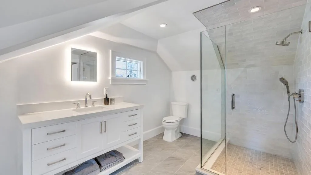 A bright bathroom with a white vanity, toilet, and glass shower.