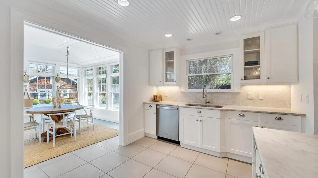 A bright white kitchen with a central window and an adjoining dining area.