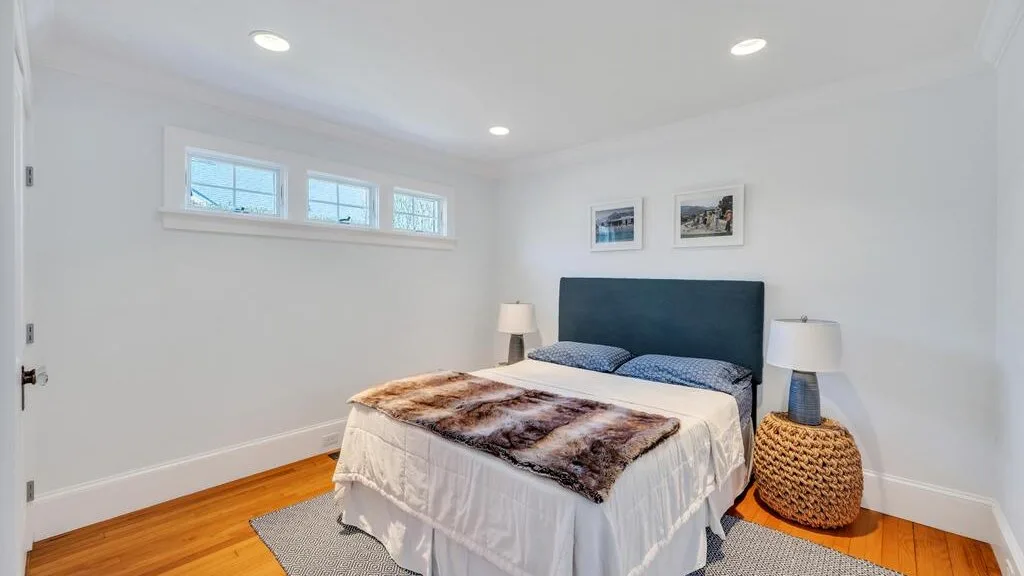 A bright bedroom with a bed, bedside lamps, and small high windows.