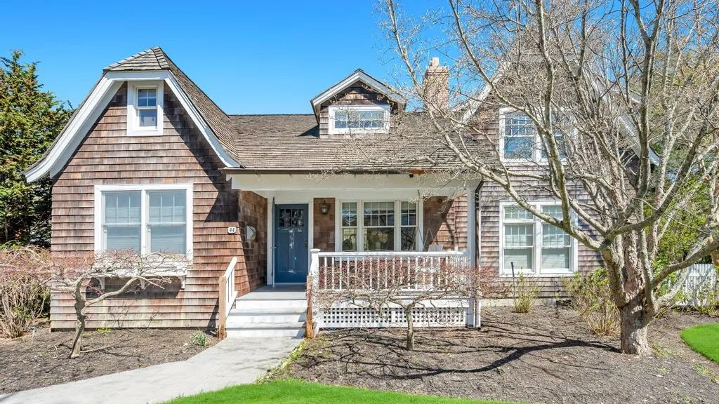 A two-story house with a covered porch and bare trees in the yard.