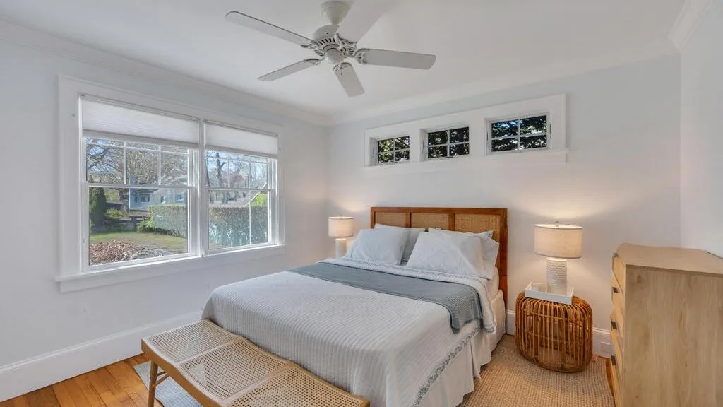 A bright bedroom with a bed beneath a ceiling fan and windows.
