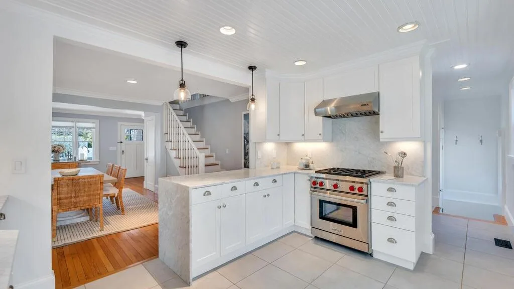 A bright kitchen with white cabinets, an oven, and an island beside a dining area.