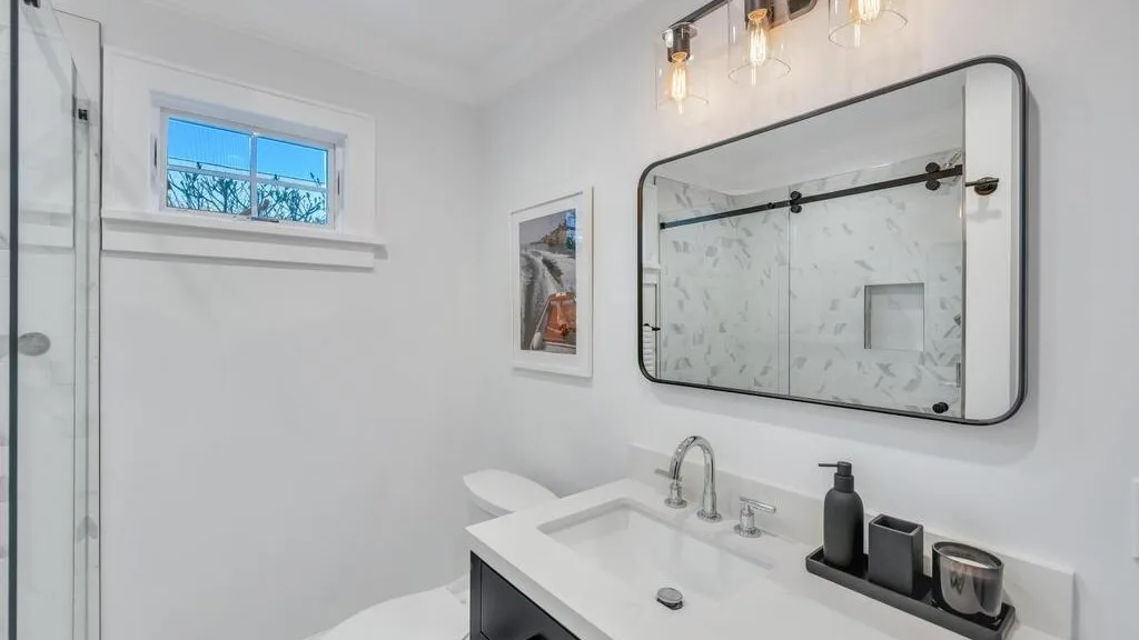A bright bathroom with a sink, mirror, and glass shower.