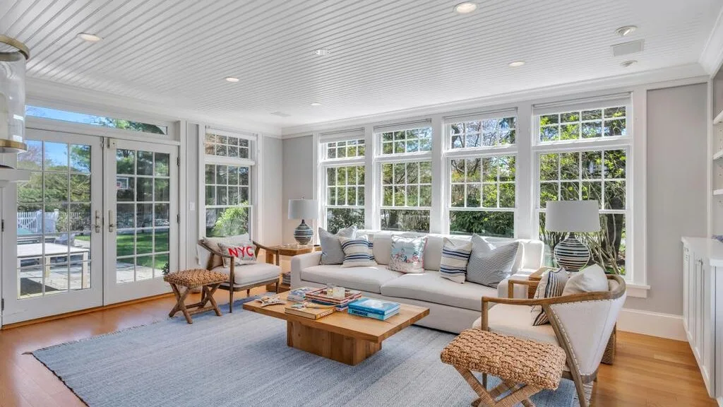 Una sala luminosa con grandes ventanas, asientos y una mesa baja de madera.