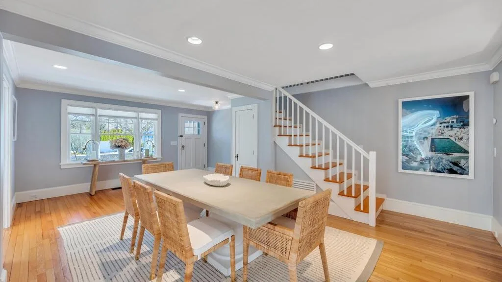 A dining area with a large table and wooden chairs beside a staircase.