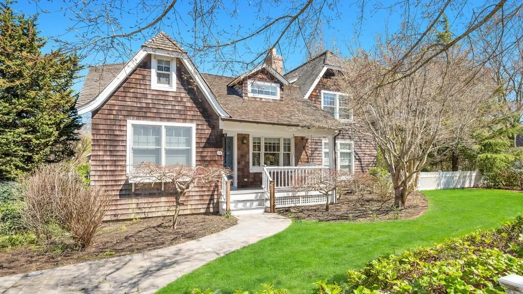 A shingled house with a small porch sits beside a green lawn.
