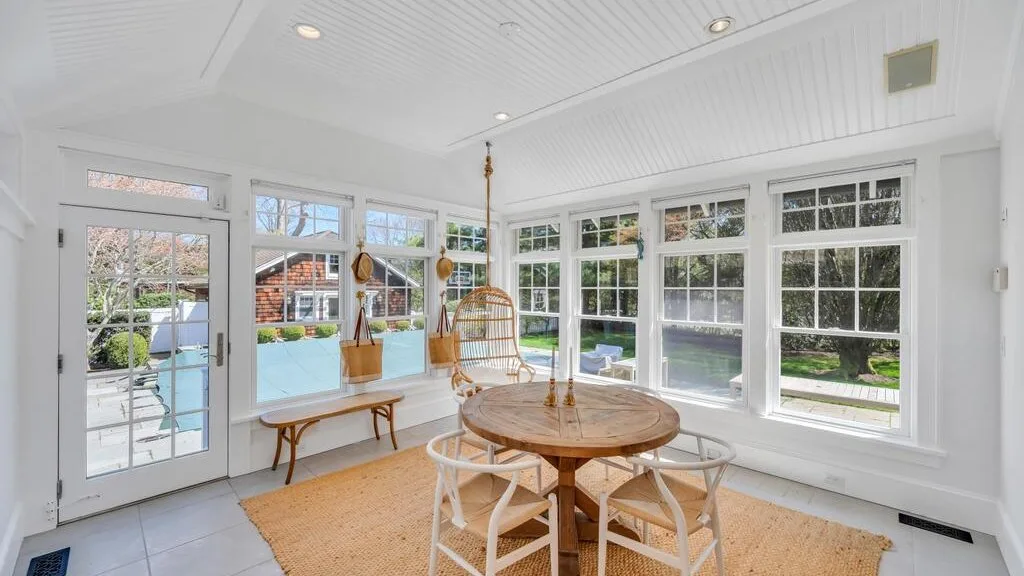 A bright sunroom with large windows and a round wooden table.