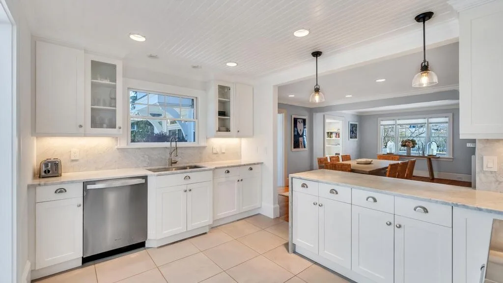 A bright kitchen with white cabinetry, a central island, and a dining area beyond.