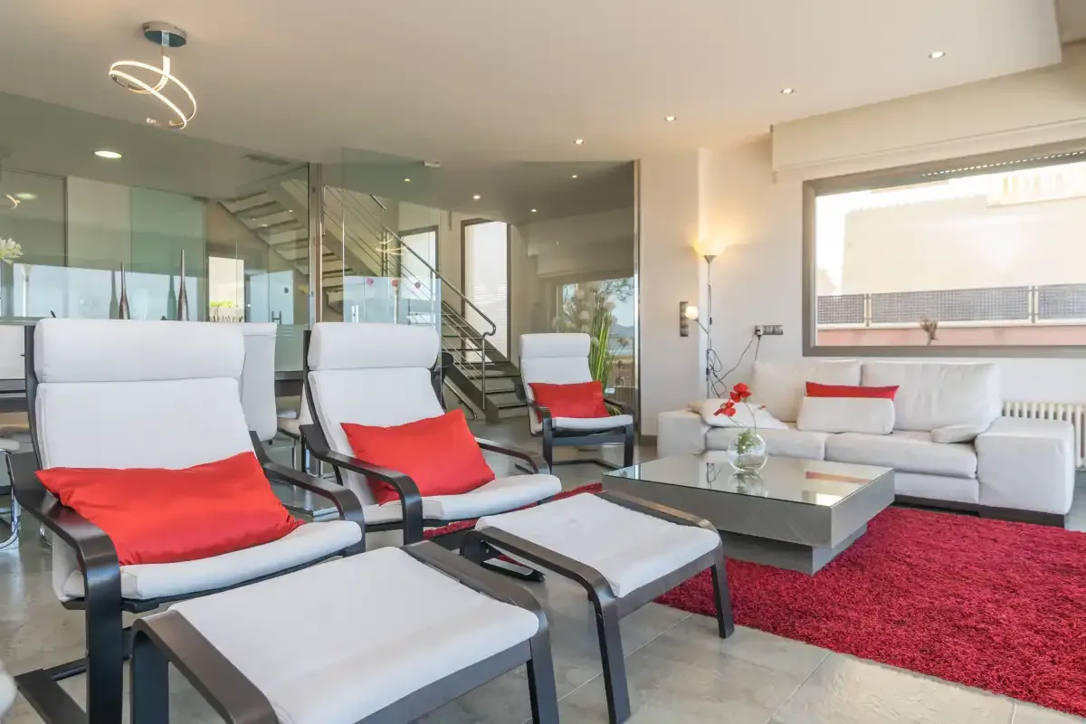 A modern living room with lounge seating, a glass coffee table, and a red rug.