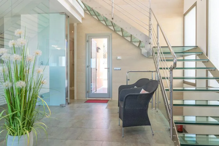 A bright entryway with a glass staircase and dark seating.