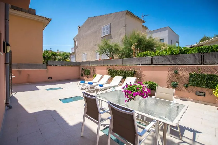 A sunny outdoor patio with a glass dining table, seating, and a small pool.