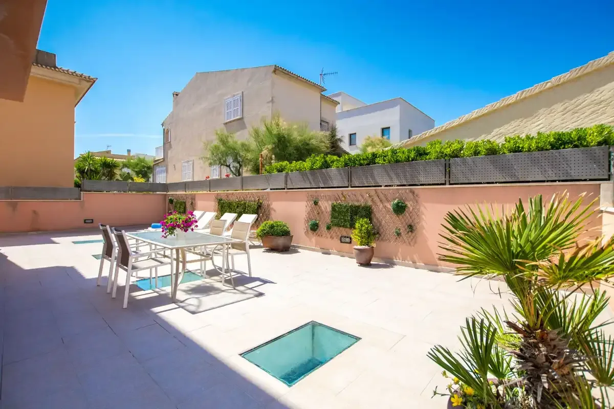 A sunny outdoor patio with a dining table, chairs, and potted plants.