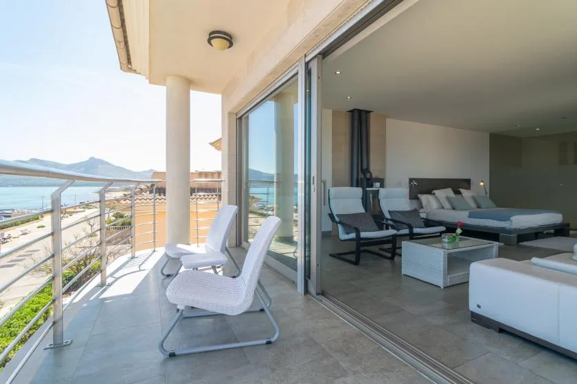 A seaside balcony with outdoor seating opens onto a living room.