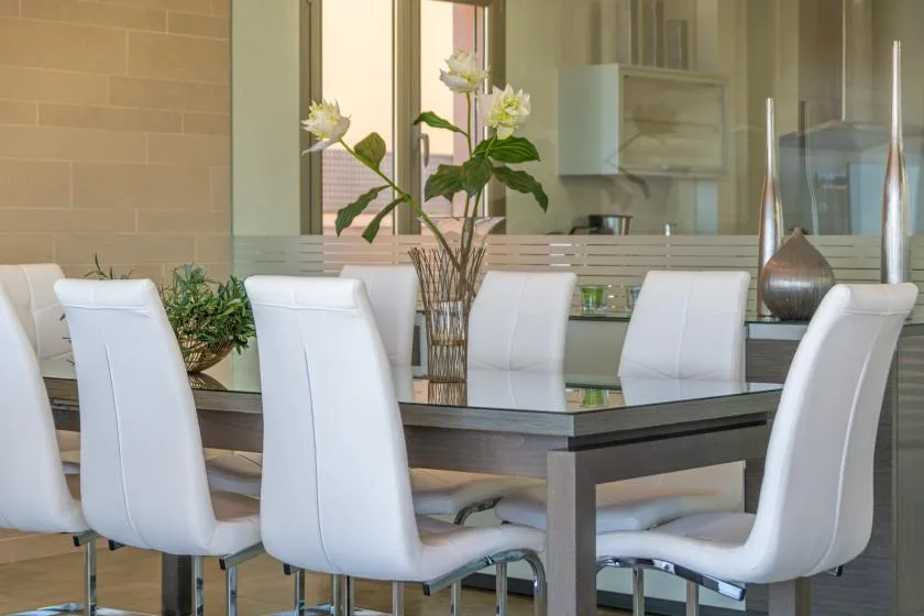 A dining area features a glass-topped table surrounded by white seating.