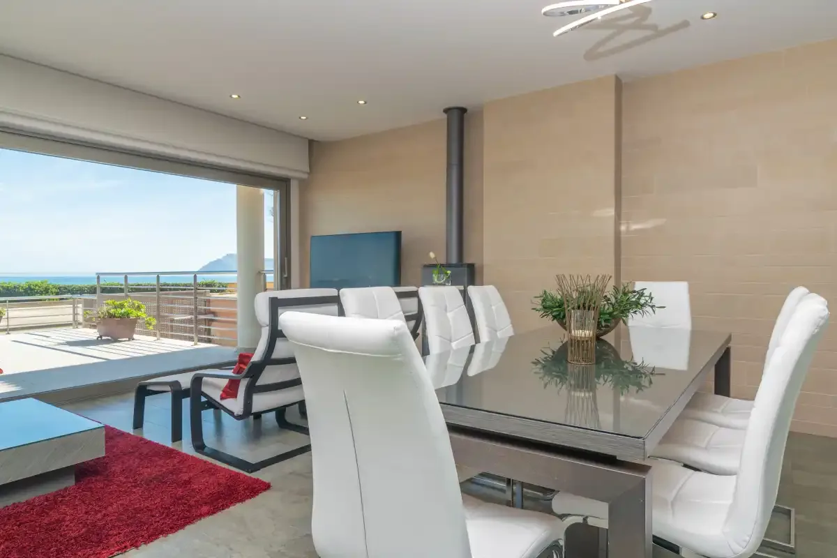 A dining area with white seating and glass doors opening to a terrace.