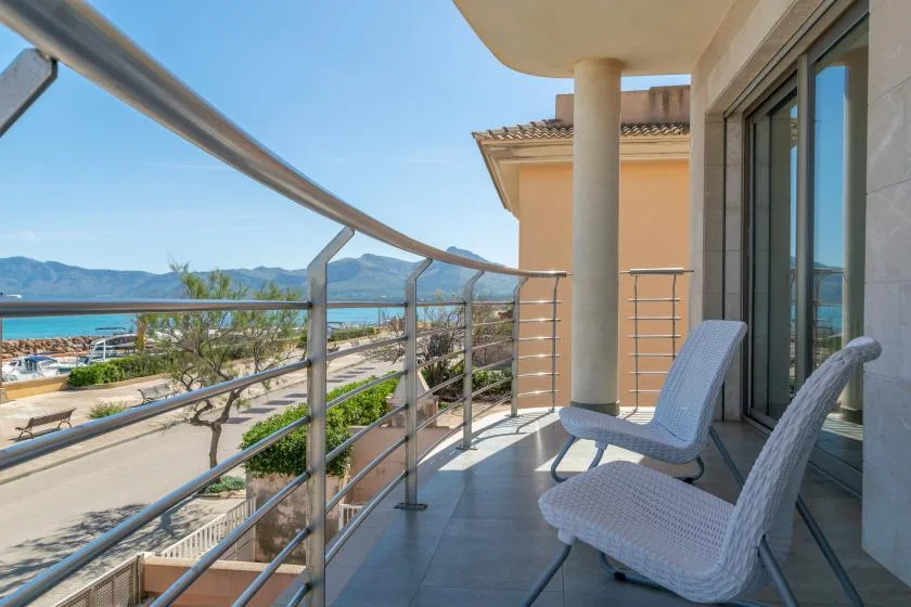 A balcony with seating overlooks the coastline and distant mountains.