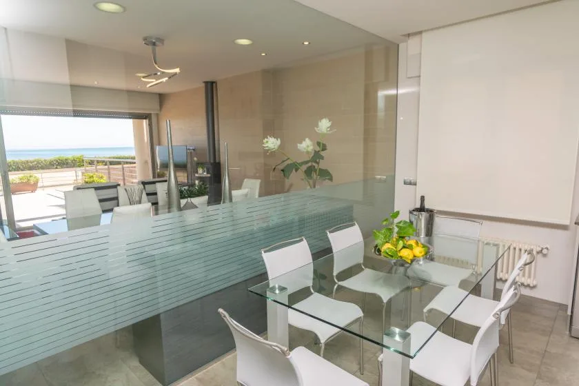 A bright dining area with a glass table and white seating beside a large window.