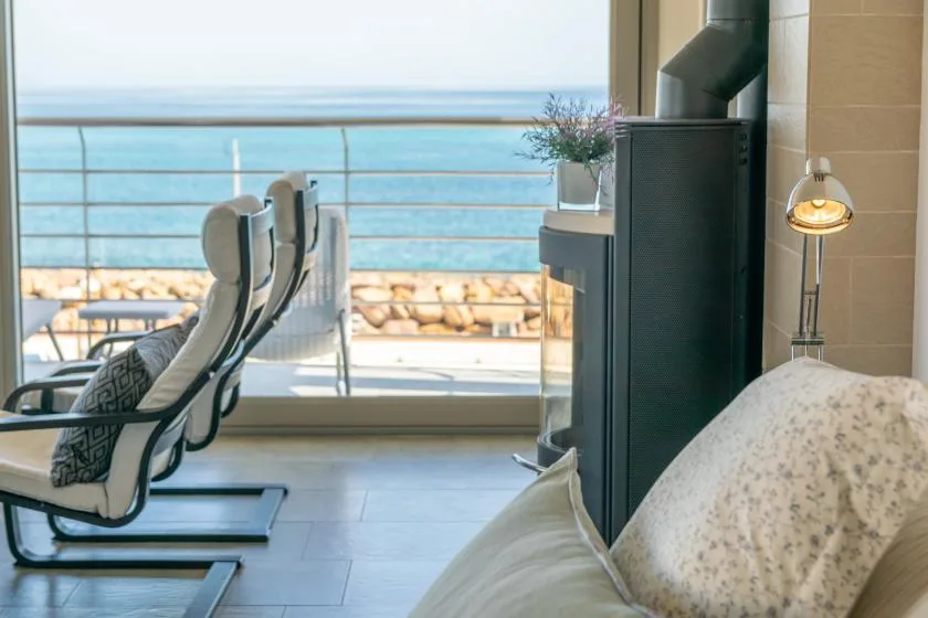 A bright living area faces the sea through wide glass doors, with seating nearby.
