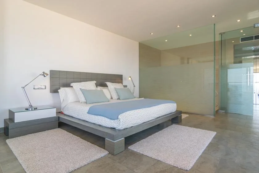 A bedroom with a large bed, bedside tables, and glass partitions.