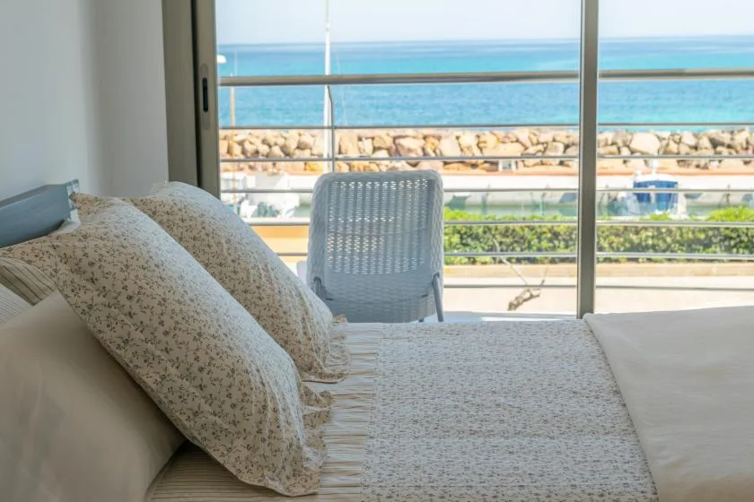 A bedroom with a bed beside a window overlooking the sea.