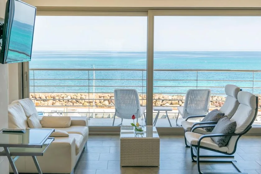 A bright living room opens onto a balcony with a view of the sea.