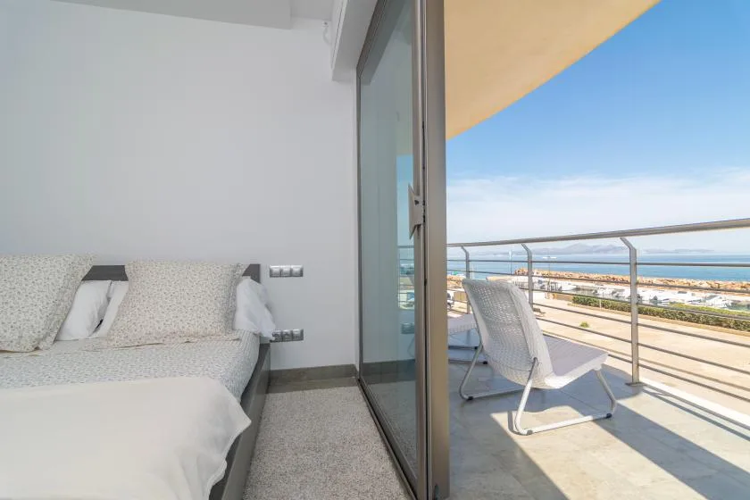 A bedroom opens onto a balcony with seating and a view of the sea.