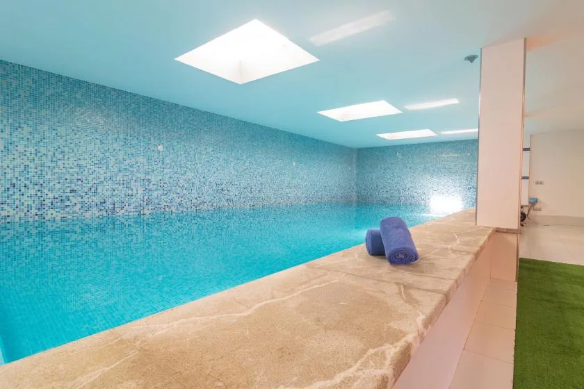 An indoor swimming pool with blue tiled walls and a stone-colored deck.
