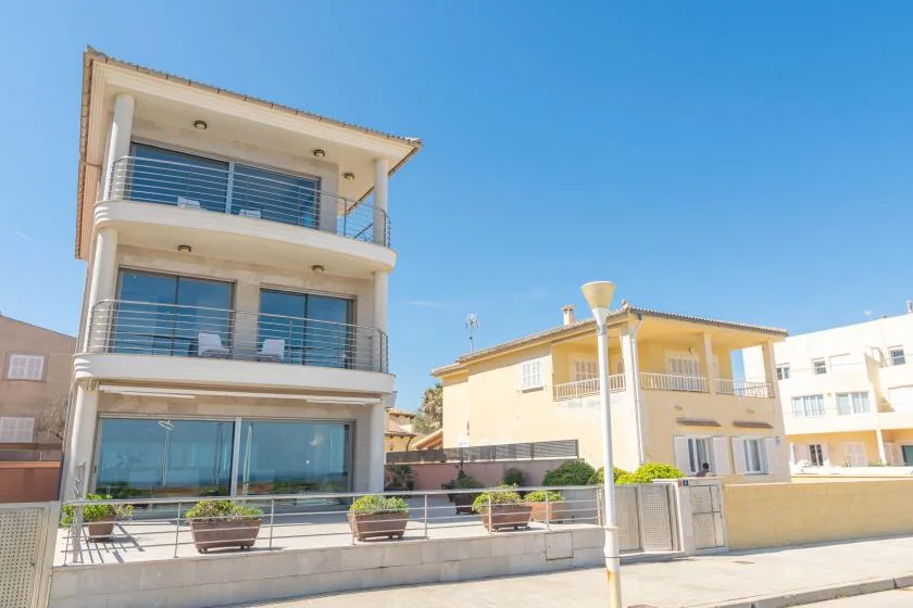 Modern multi-story building with glass balconies beside a yellow building under a clear sky.