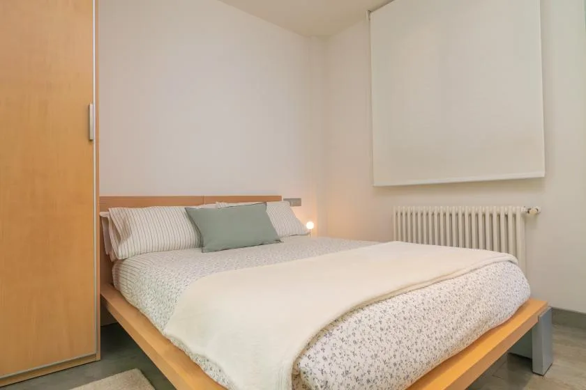 A bedroom with a neatly made bed and a radiator along the wall.
