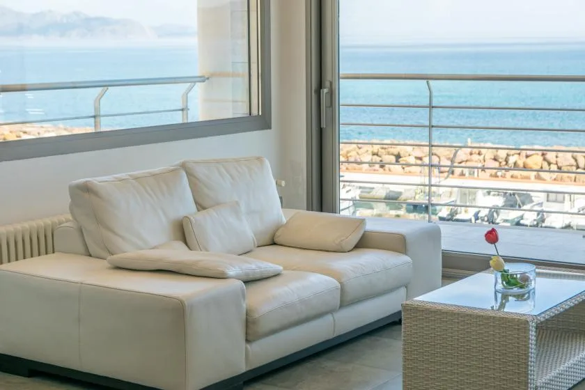 A living room with light-colored seating beside large windows overlooking the water.