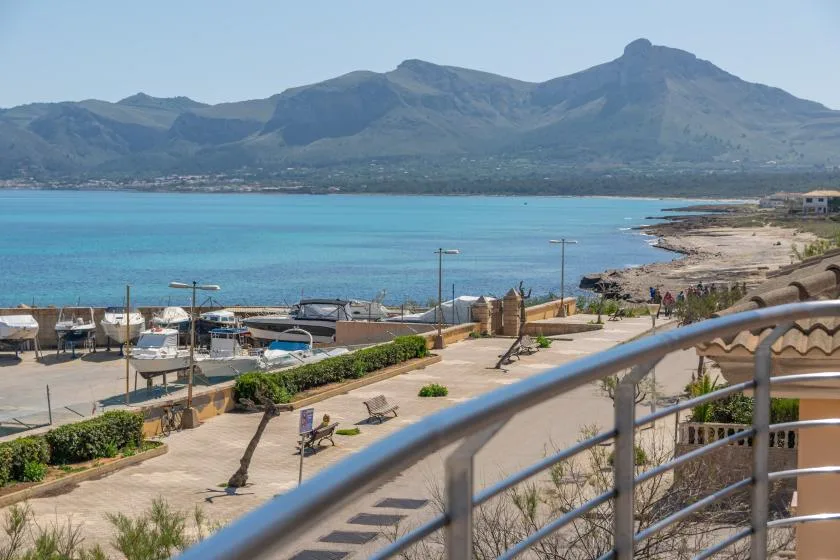 A waterfront promenade overlooks a turquoise bay and distant mountains.