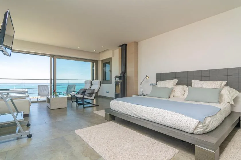 A bedroom with a large bed and seating beside floor-to-ceiling windows.