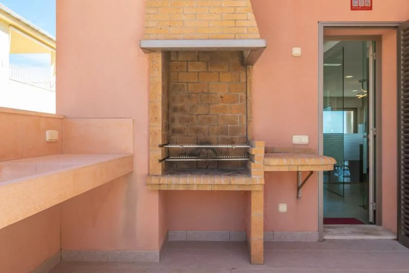 A covered patio with a built-in brick grill and an open doorway.