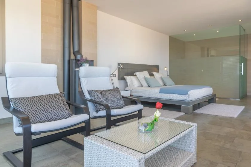 A bedroom with a low bed, two lounge chairs, and a glass-topped table.