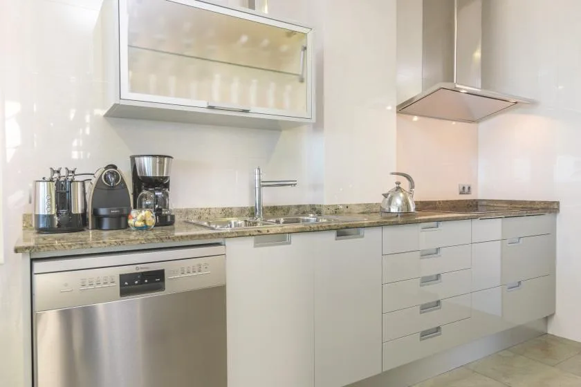 A bright modern kitchen with a long counter, stainless steel appliances, and a kettle.