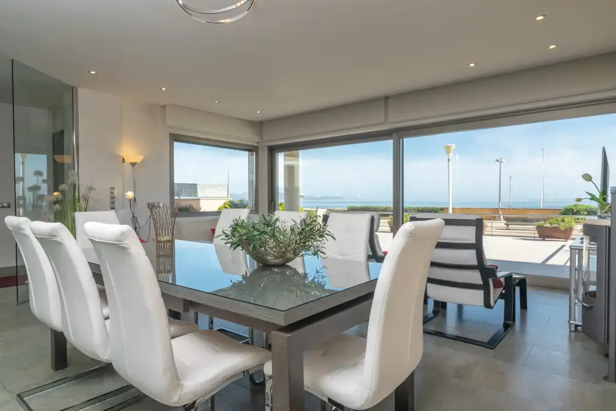A dining area with white seating and large windows overlooking the sea.