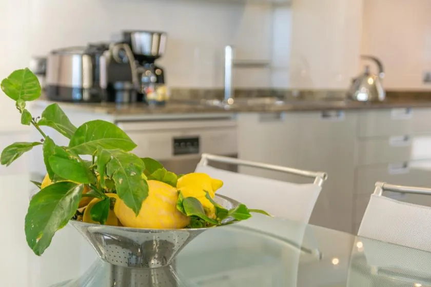 A kitchen with a glass dining table and a bowl of lemons.