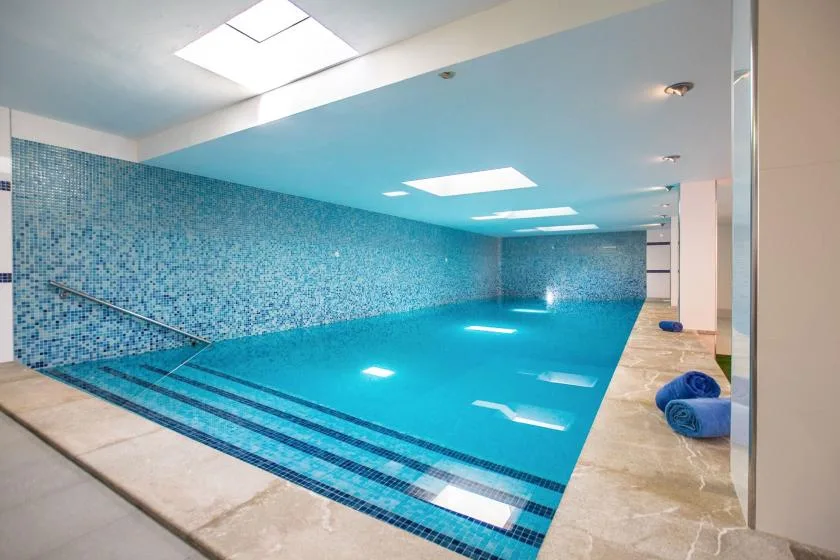An indoor swimming pool with blue mosaic walls and tiled walkways.