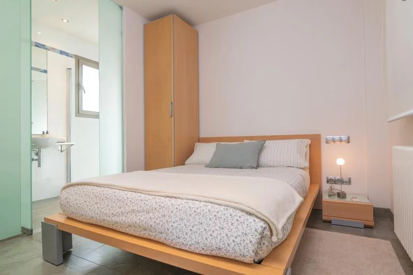 A bedroom with a neatly made bed and a wardrobe beside a glass bathroom partition.