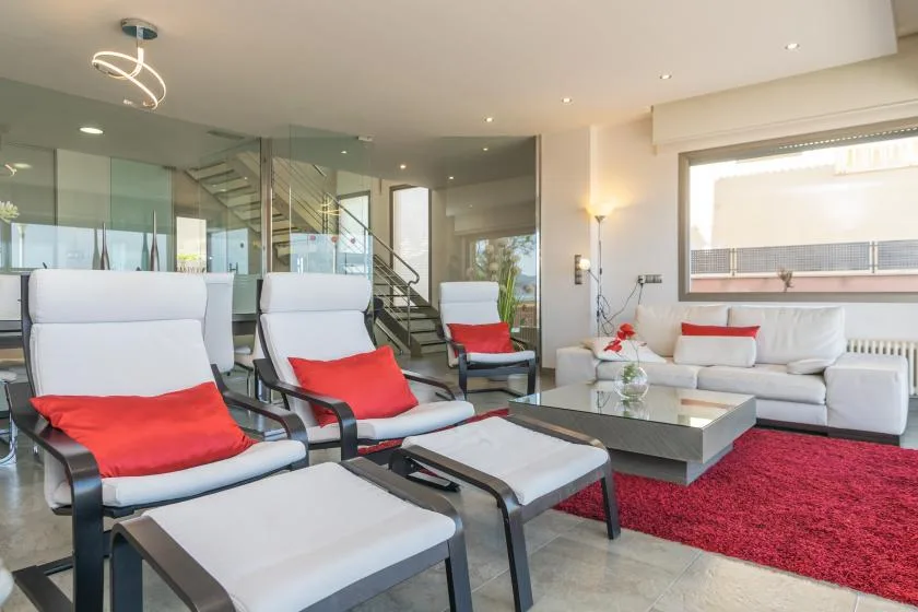 A modern living room with white seating, red cushions, and a glass coffee table.