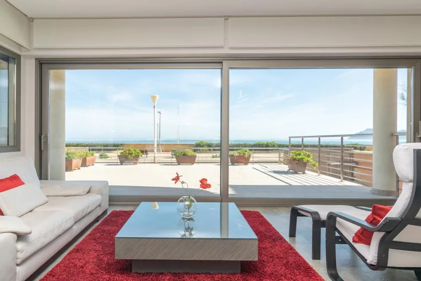 A bright living room opens onto a terrace through wide glass doors.