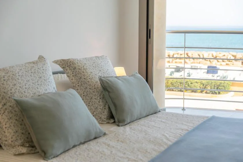 A bedroom seating area with pale cushions beside a large window overlooking the sea.