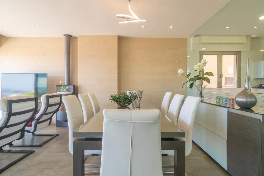 A modern dining area with white seating, a long table, and a mirrored wall.